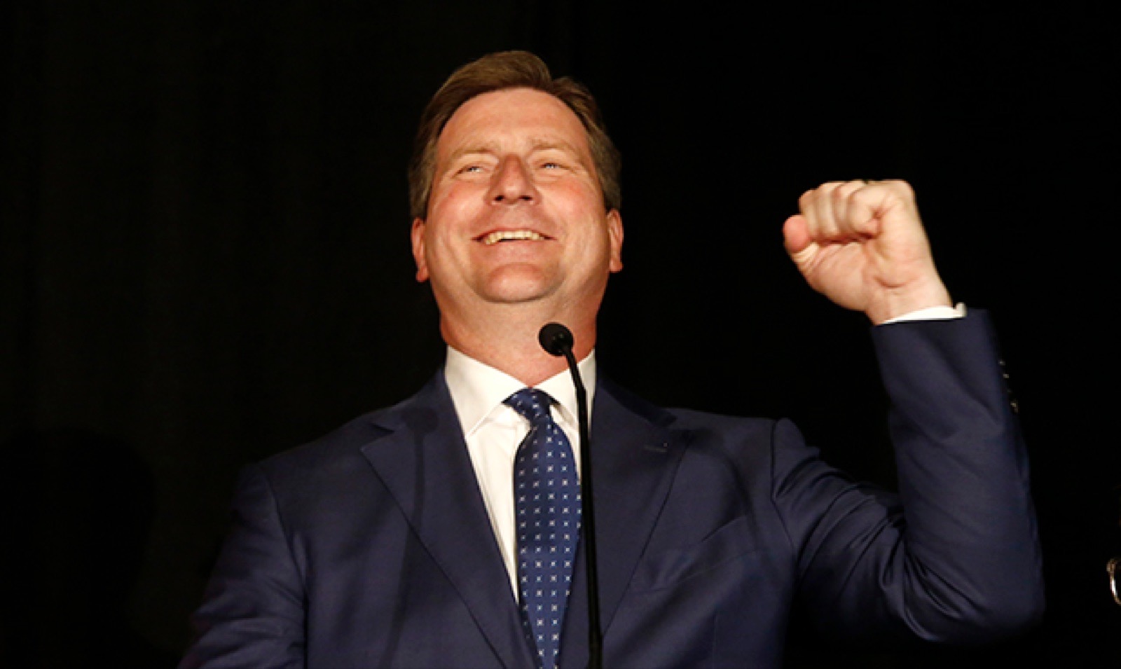 Greg Stanton celebrating with a raised fist at an election night podium